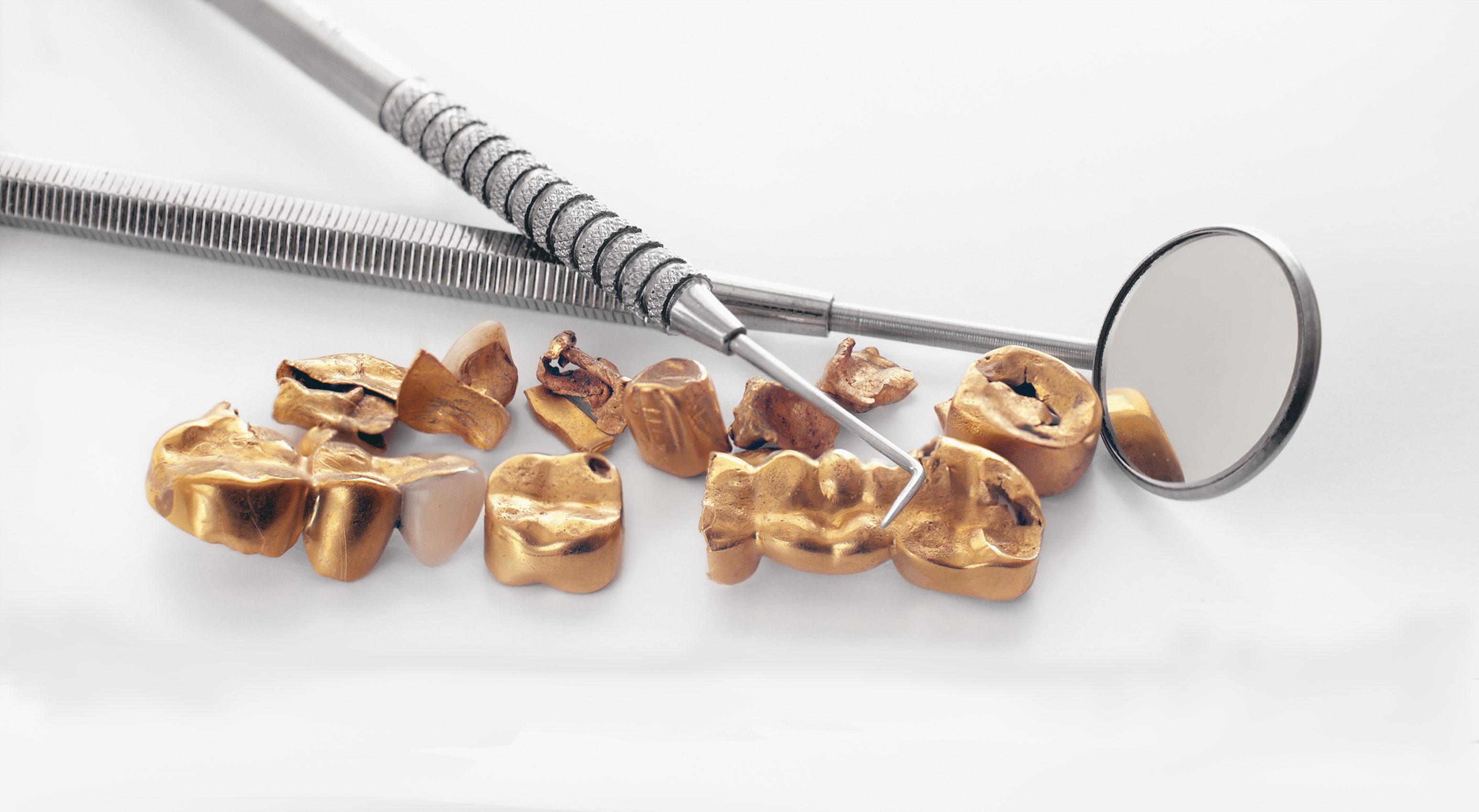 Dental exam tools laid behind an assortment of gold dental bridges