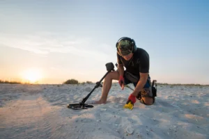 A man with a metal detector searching for buried gold digs into the sand on a beach
