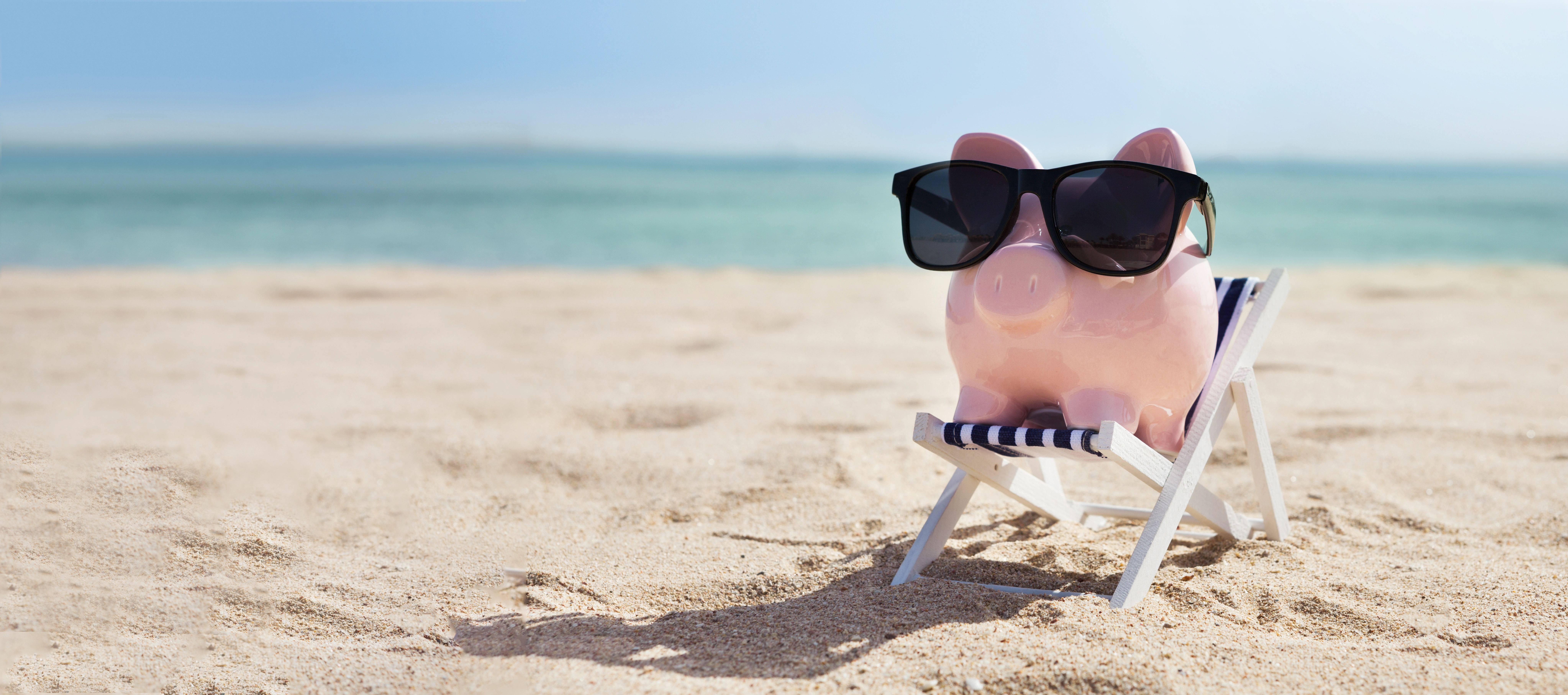 Pink Piggybank Wearing Eyeglasses On Deck Chair Over The Sandy Beach