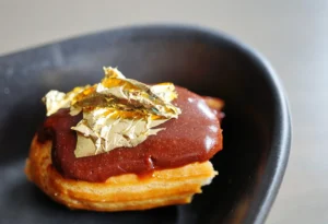 Bite of a chocolate eclair pastry with an edible gold leaf on top