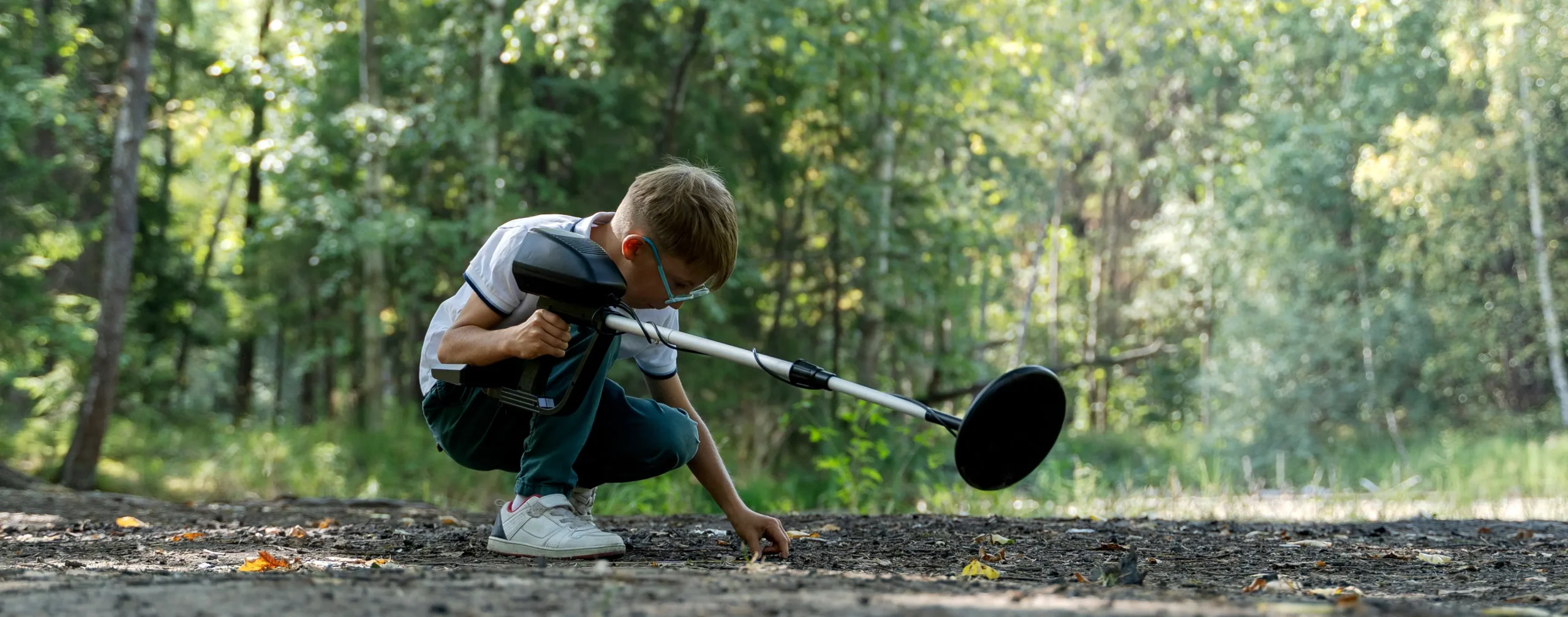 A young boy inspects the forest floor while metal detecting for buried precious metals