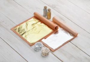 Natural edible food gold and silver sheets, flakes and powder on white wooden table