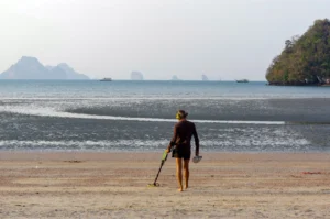 A man uses a metal detector on the shoreline of a beach in Southeast Asia