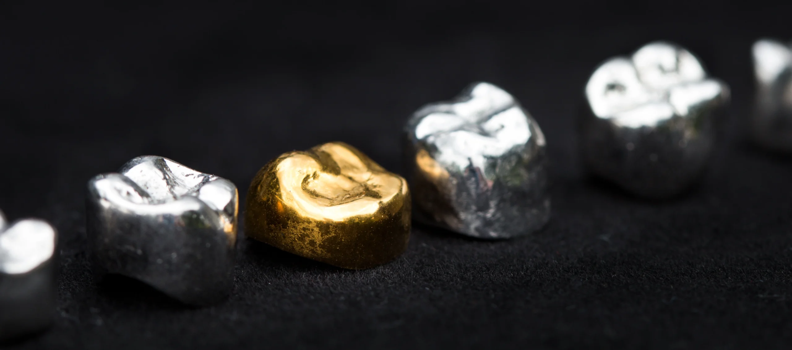 6 gold dental crowns lined up on a black background