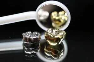 two gold dental crowns in front of a dental mirror tool on a black background