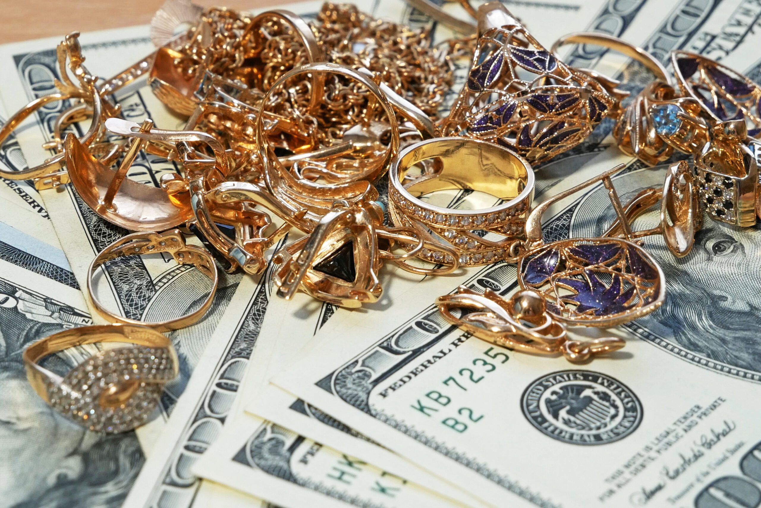 Assorted gold and other precious metal scrap and jewelry laid over $100 US bills