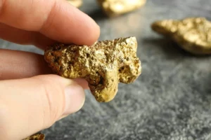 Hand holding gold nugget at grey textured table